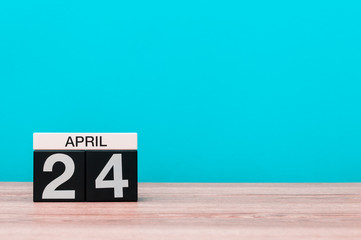 April 24th. Day 24 of month, calendar on wooden table and turquoise background. Spring time, empty space for text