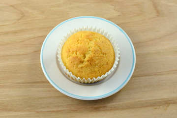 One cornbread muffin in paper muffin cup on small bread plate