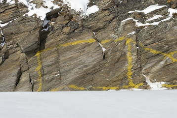 Yellow rectangle painted on a rock of mountain in a mountaineering path. Sign / symbol on a mountain path in winter with rock covered with snow, Simplon Pass, Alps, Switzerland