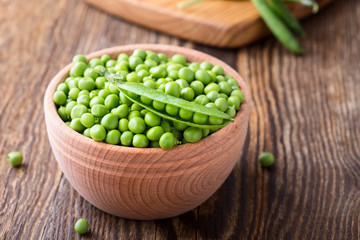 Green peas in wooden bowl on  rural background