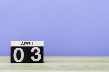 April 3rd. Day 3 of month, calendar on wooden table and purple background. Spring time, empty space for text