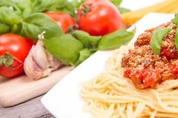 Spaghetti bolognese,some tomatoes, olive oil, basil, garlic, and raw pasta in the background