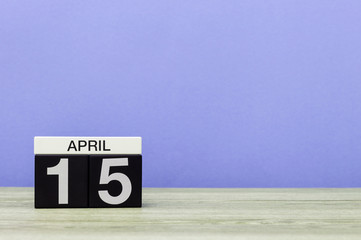 April 15th. Day 15 of month, calendar on wooden table and purple background. Spring time, empty space for text