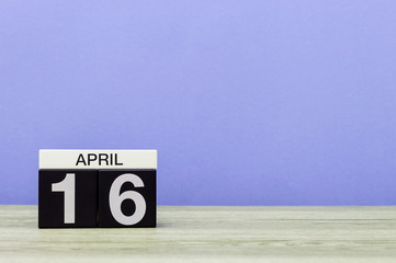 April 16th. Day 16 of month, calendar on wooden table and purple background. Spring time, empty space for text
