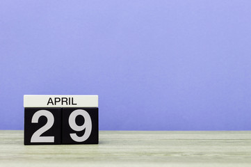 April 29th. Day 29 of month, calendar on wooden table and purple background. Spring time, empty space for text