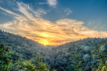 Fototapeta na wymiar Mountain forest landscape under evening sky with clouds in sunlight. Majestic sunset in indian Himalaya mountains. HDR image.