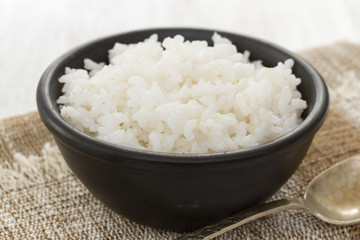 boiled rice in black bowl in wooden background