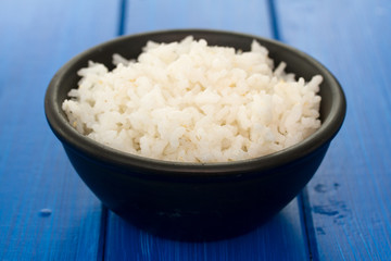 boiled rice in black bowl in wooden background