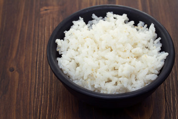 boiled rice in black bowl in wooden background