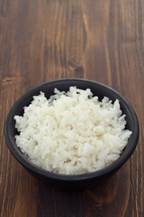 boiled rice in black bowl in wooden background