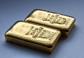 Two cast gold bars weighing 250 grams on a blue background. Selective focus.