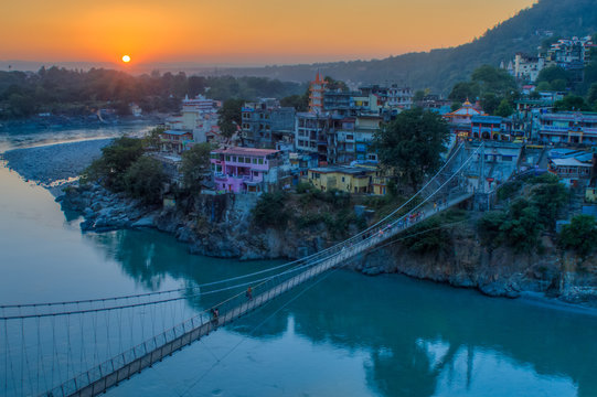 View Of River Ganga And Lakshman Jhula Bridge At Sunset With A Blue Sky And Colorful Houses. Rishikesh. India. HDR Image