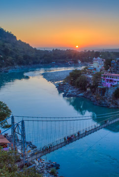 View of River Ganga and Lakshman Jhula bridge at sunset with a blue sky and colorful houses. Rishikesh. India. HDR image