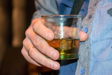 Man is holding a glass of scotch whiskey with ice