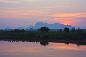 Fototapeta na wymiar Colorful tropical sunset. Rice feilds and mountains reflecting in the water.