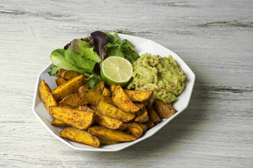 Spicy potato wedges with guacamole, green salad and lime