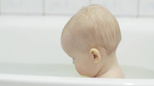 Cute little towheaded European child takes a bath with foam close-up, side view