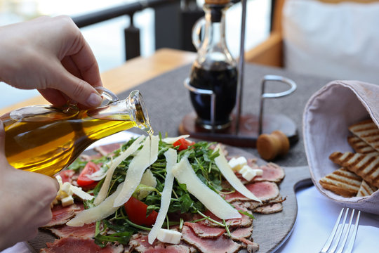 Woman adding olive oil into fresh salad. Carpaccio , beef steak salad. Summer launch, healthy eating concept