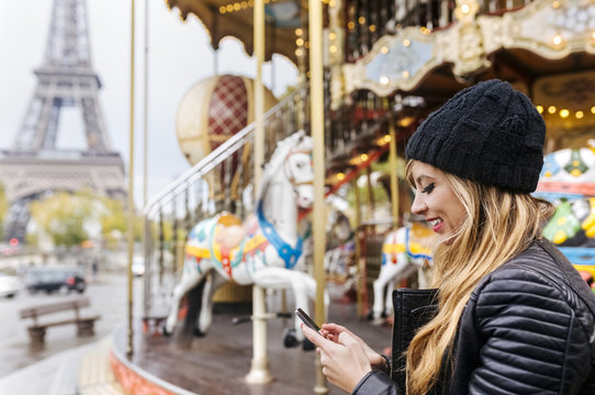 France, Paris, young woman using her smartphone with a carousel and the Eiffel Tower in the background