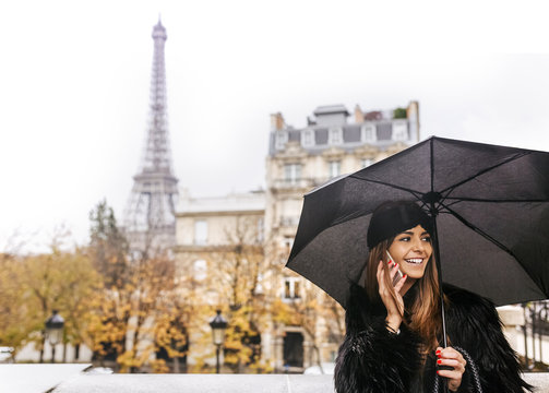 France, Paris, young woman talking on cell phone under umbrella with the Eiffel Tower in the background