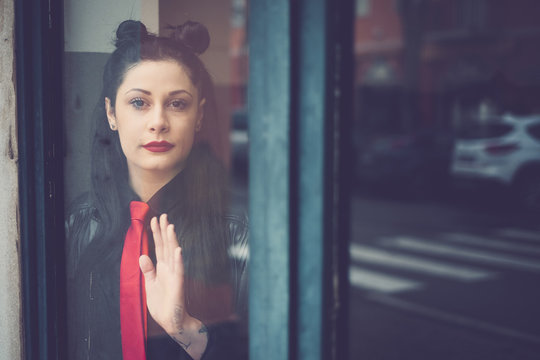 Portrait of dark-haired young woman wearing red tie standing behind glass door