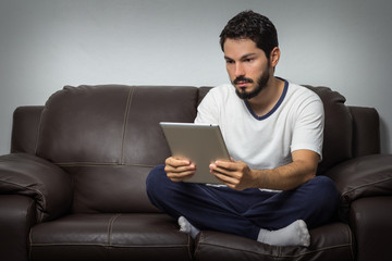 Guy on a sofa, at home, with a tablet in hands