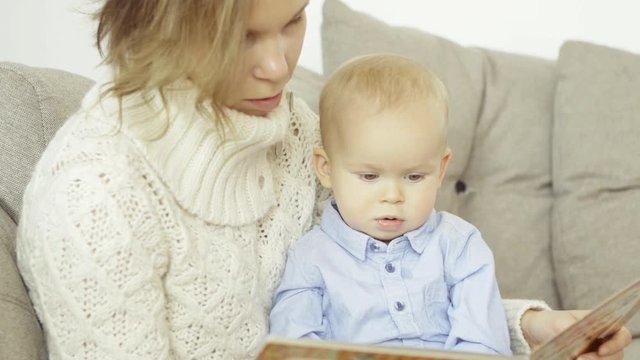 Portrait of a European mother and son reading a children's interesting book, sitting on the couch