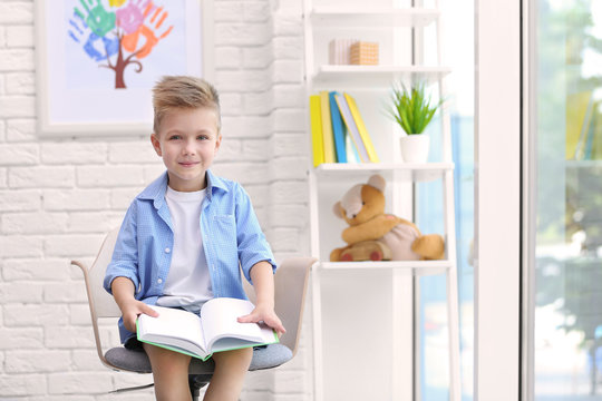 Cute Boy Sitting On Chair And Reading Book