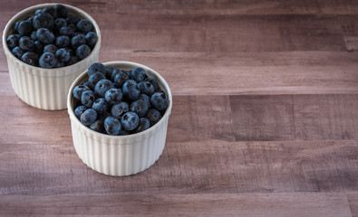Fresh tasty blueberries in two white ceramic, porcelain bowls on wooden table, surface, rustic style. Antioxidant organic superfood