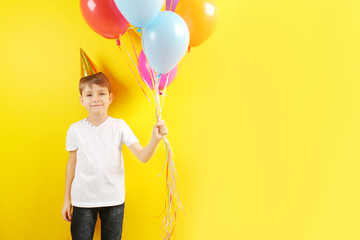 Cute birthday boy with colorful balloons on yellow background