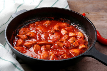 Frying pan with delicious chicken tikka masala on wooden table