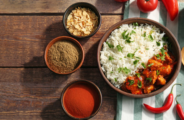 Bowl with delicious chicken tikka masala, rice and spices on wooden table