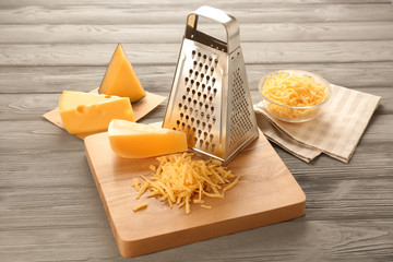 Grater and cheese on wooden board