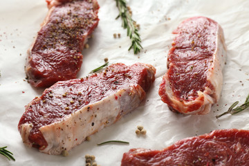 Raw steaks with rosemary and spices on parchment