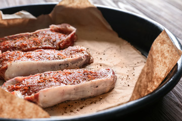 Raw steaks with spices on parchment in baking dish