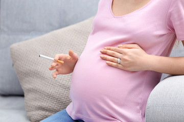 Pregnant woman smoking cigarette sitting on sofa at home