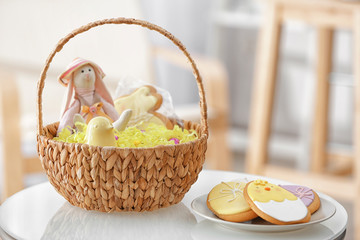 Easter basket with decorations and plate with delicious cookies on blurred background