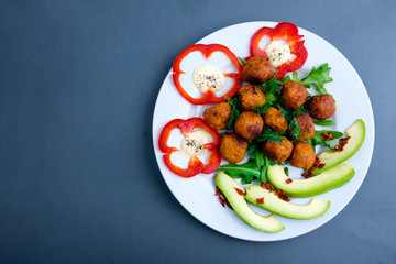 Vegetarian falafels and vegetables on a plate. With pepper and herbs and avocado