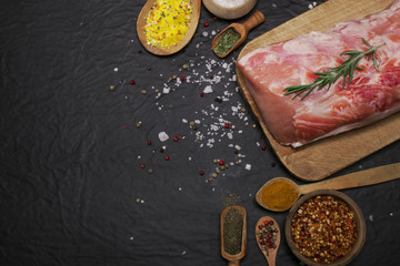 Raw pork meat on a cutting board with rosemary and spices.