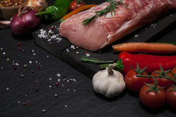 Raw pork meat on a cutting board with rosemary, vegetables and spices.