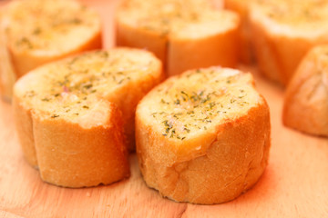 Slices of crunchy garlic bread on wooden plate.