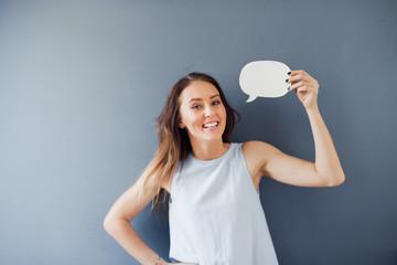 Smiling young woman posing with a speech bubble against a gray background.