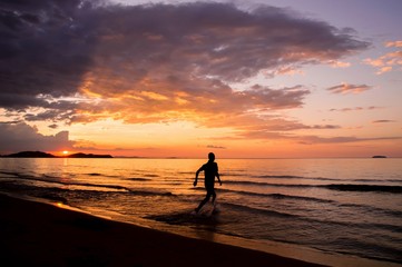 Silhouette of happy man running on the beach at sunset