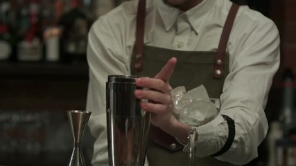 Barman hands pouring liquid to shaker, shaking and mixing alcohol cocktail in bar interior