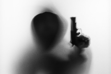 Shadow blur of horror man in jacket with hood gun in his hand.Dangerous man behind the frosted glass.Mystery man.Halloween background.Black and white picture.Blur picture.