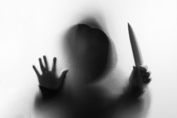Shadow blur of horror man in jacket with hood knife in his hand.Dangerous man behind the frosted...