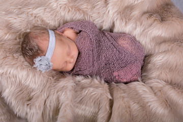 Beautiful newborn baby girl swaddled and sleeping on fur