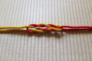 日本の伝統工芸品の赤と黄の２本の組紐が畳の上にある