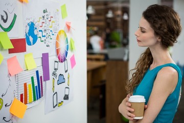 Thoughtful female executive looking at sticky notes on white wall