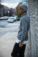 A young, hip man poses for a pensive portrait along a fence in NYC